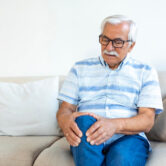 Person holding knee while standing up from office chair — knee pain after sitting